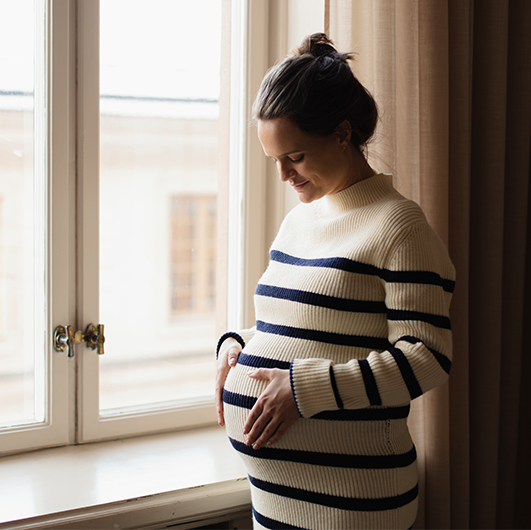 Gravid kvinna i randig klänning som håller händerna runt magen