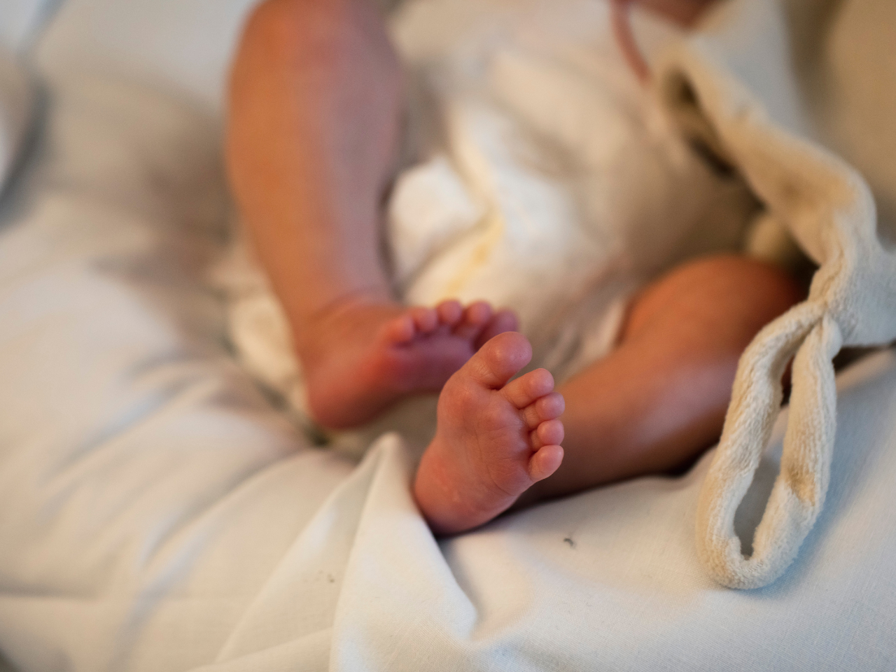 Nyfödd babys fötter på vit filt, resultat av trygg förlossning med värktimer.